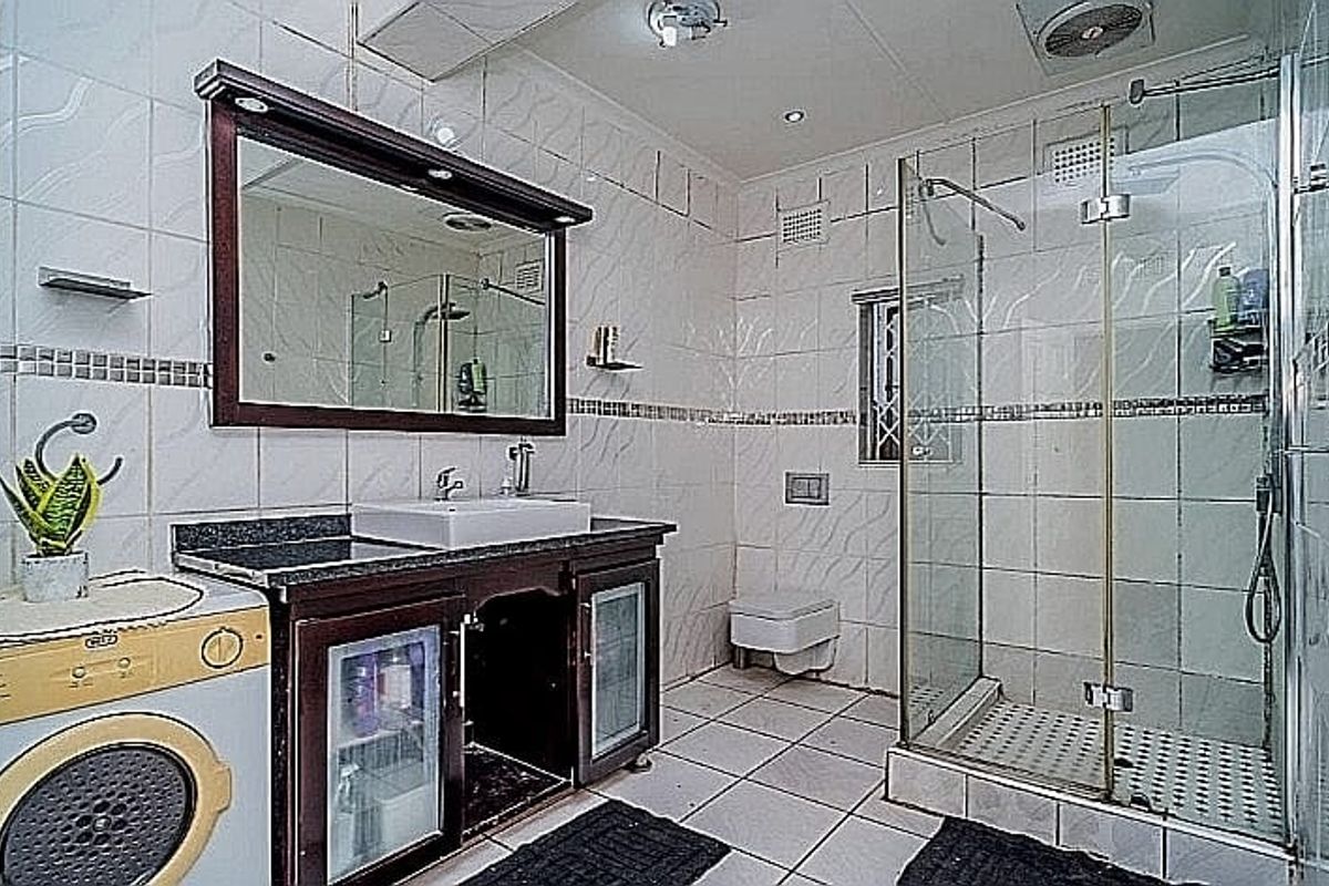 A functional bathroom featuring a vanity with a vessel sink, a glass-enclosed shower, and a wall-hung toilet, finished with tiled surfaces throughout.