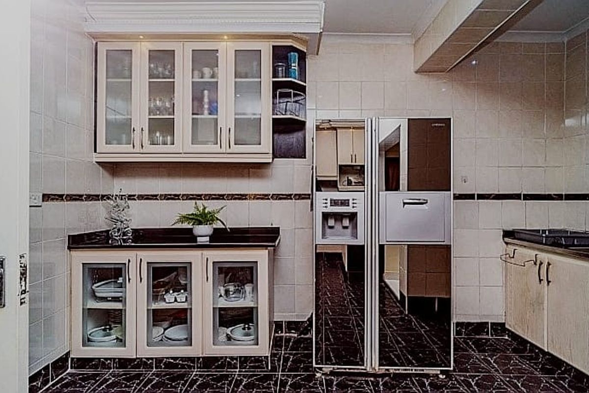 A functional kitchen featuring built-in cabinetry, stone countertops, tiled wall finishes, and a large integrated refrigerator, offering a practical layout for food preparation.