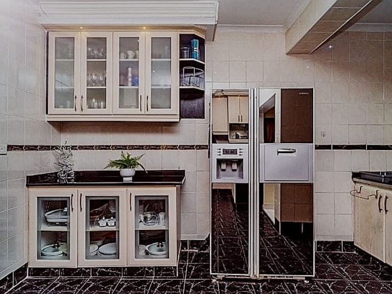 A functional kitchen featuring built-in cabinetry, stone countertops, tiled wall finishes, and a large integrated refrigerator, offering a practical layout for food preparation.