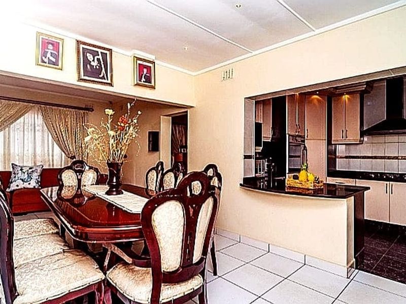 Open-plan dining area adjacent to a functional kitchen featuring built-in cabinetry, a breakfast bar, and tiled flooring throughout.