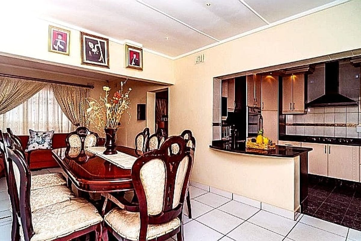 Open-plan dining area adjacent to a functional kitchen featuring built-in cabinetry, a breakfast bar, and tiled flooring throughout.