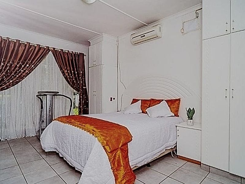 A bedroom featuring built-in cupboards, tiled flooring, and a wall-mounted split-system air conditioner.