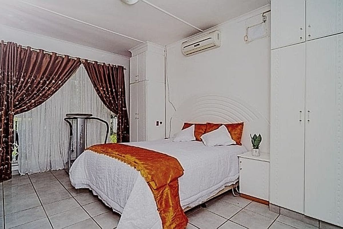 A bedroom featuring built-in cupboards, tiled flooring, and a wall-mounted split-system air conditioner.