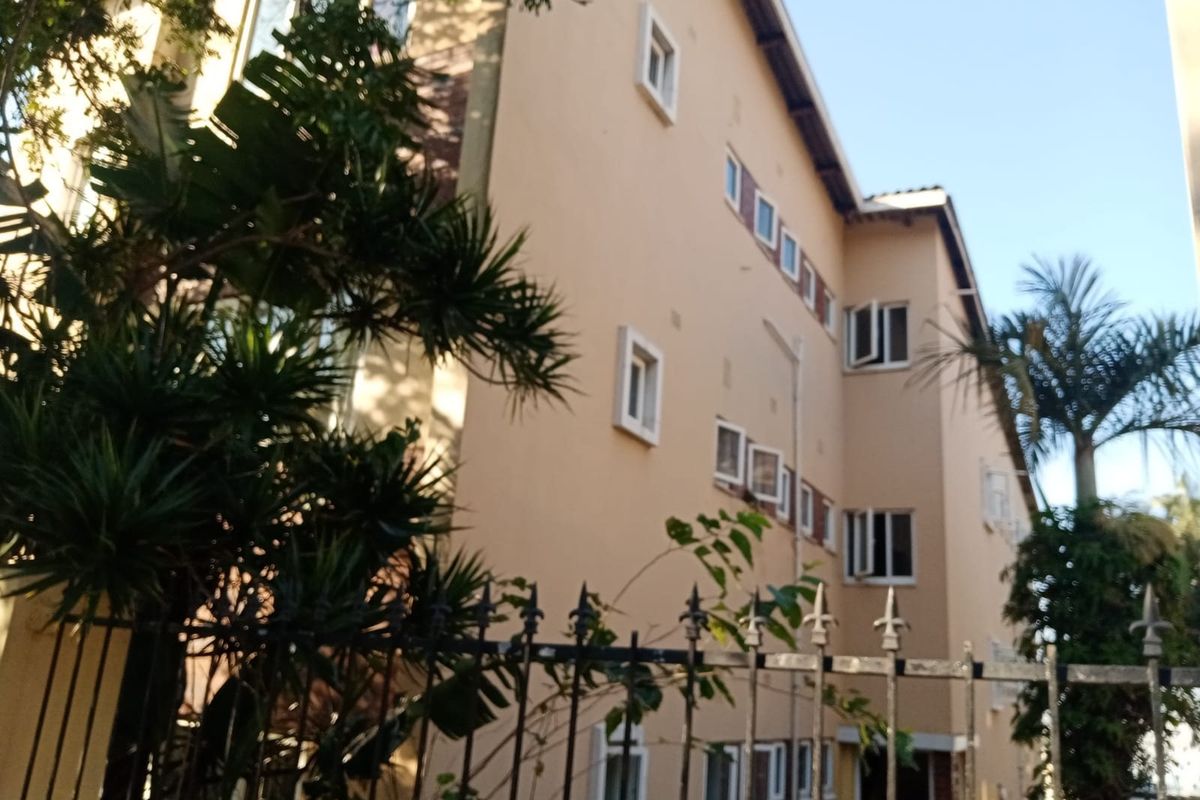 A view of the apartment building exterior featuring a multi-story facade with casement windows and metal perimeter fencing.