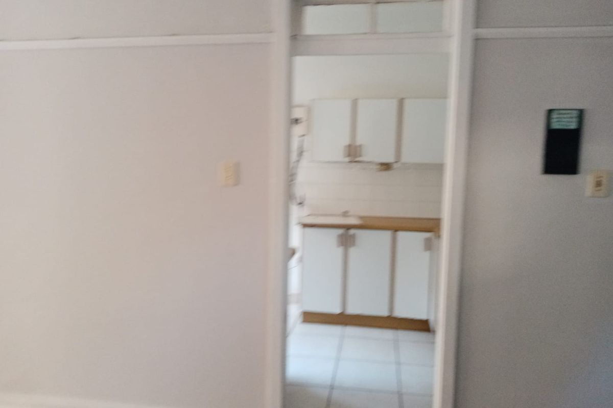 A view through a doorway into a small, empty kitchen featuring basic built-in cabinetry, a sink, and tiled flooring.