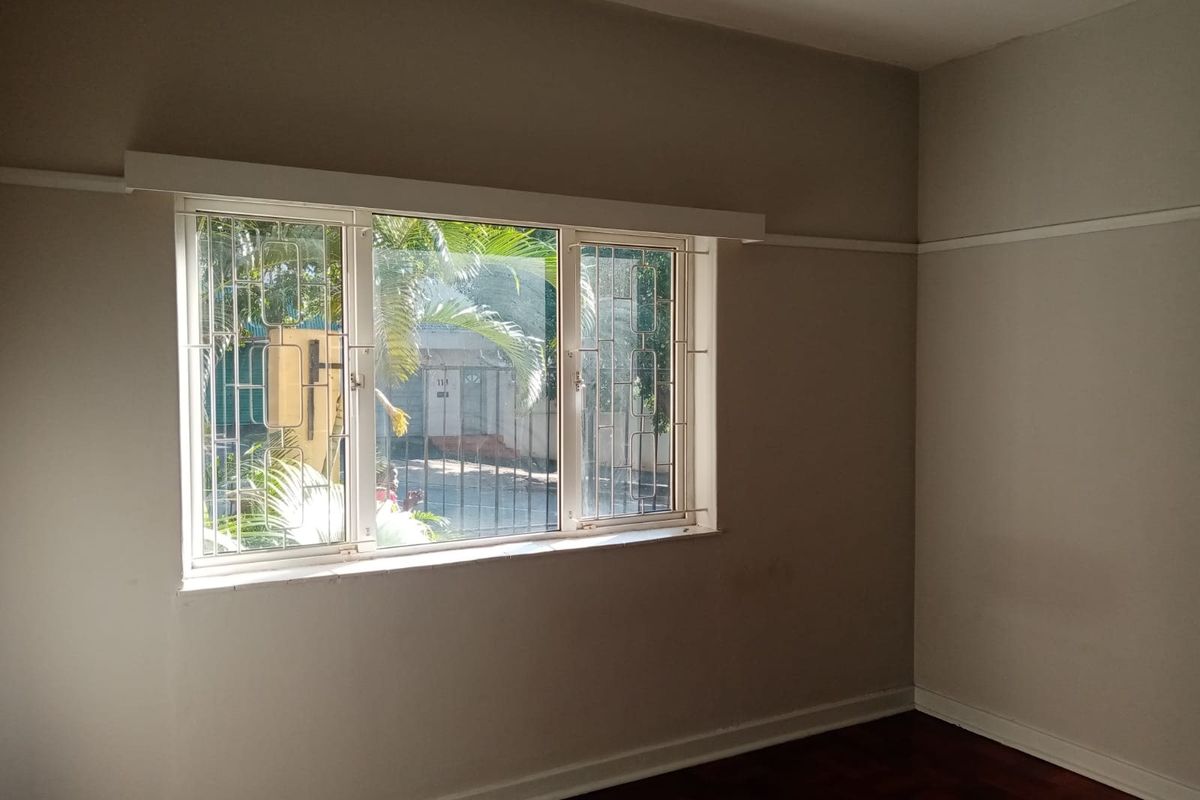 An empty bedroom featuring classic parquet flooring, a picture rail, and a window fitted with security bars.