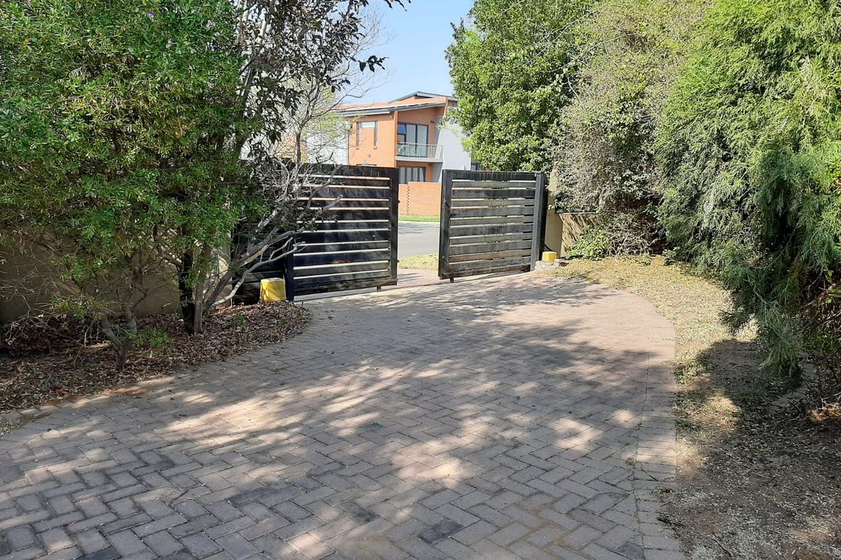 A paved driveway leading to a modern timber slat gate, surrounded by mature trees and established garden landscaping.