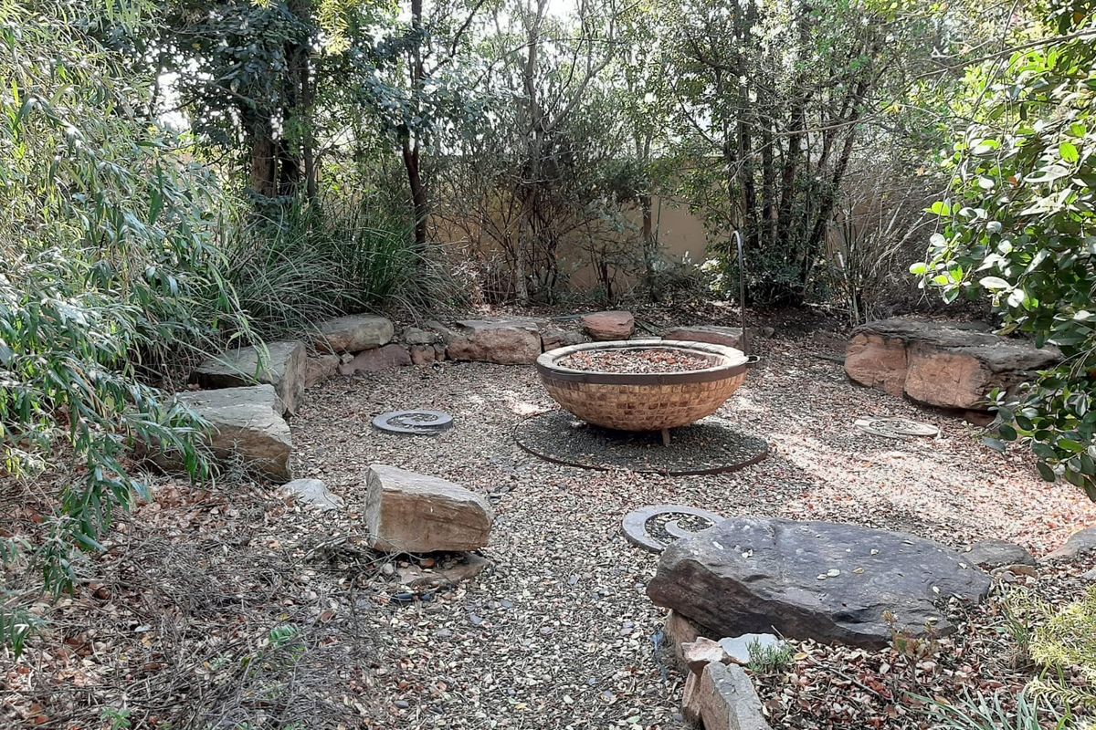 A landscaped garden area featuring a central fire pit, natural stone accents, and mature trees providing a secluded outdoor space.