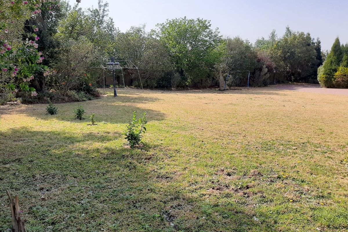 A spacious, established residential garden featuring a large lawn area surrounded by mature trees and greenery.