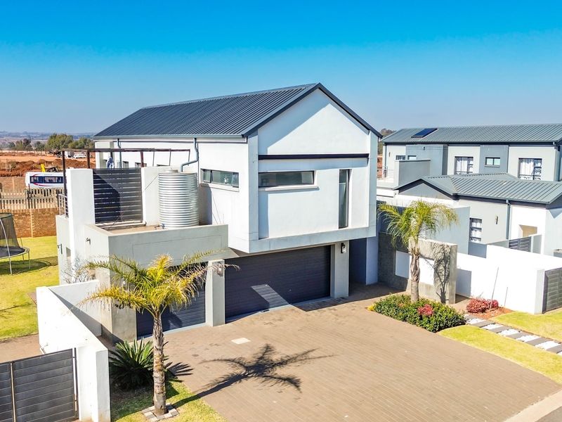Aerial view of a modern double-story residential property featuring a paved driveway, double garage, and metal roof construction.