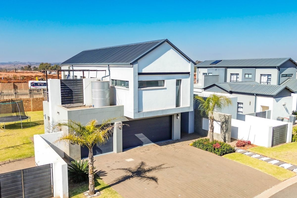 Aerial view of a modern double-story residential property featuring a paved driveway, double garage, and metal roof construction.