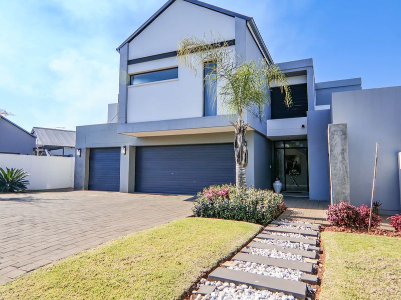 Modern double-story residential home featuring a paved driveway, double garage, and a well-maintained landscaped front garden with a stone pathway.