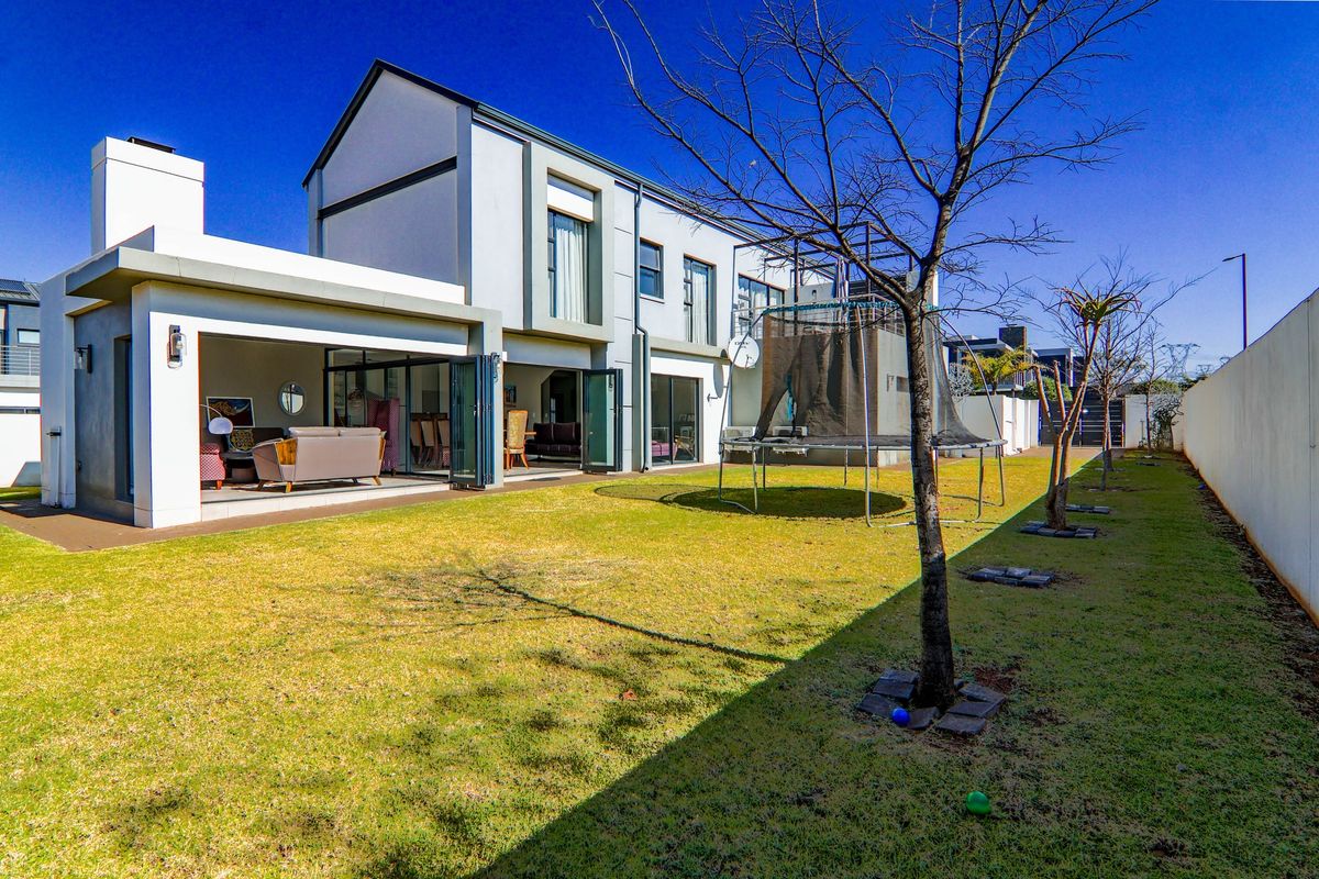 Rear view of a modern two-story house featuring a covered patio with bi-fold doors opening onto a private garden and lawn area.