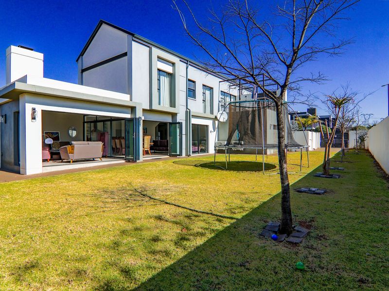 Rear view of a modern two-story house featuring a covered patio with bi-fold doors opening onto a private garden and lawn area.