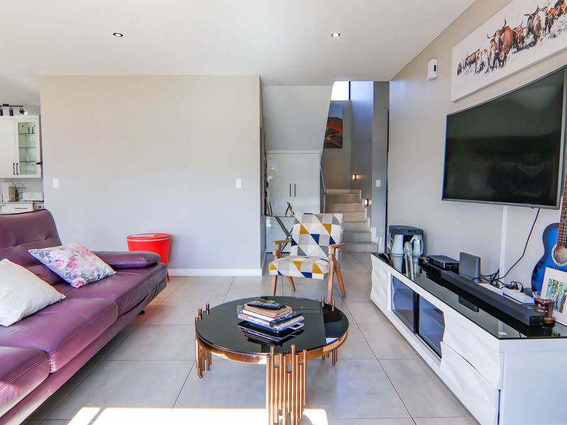 An open-plan living area featuring tiled floors, recessed lighting, and a staircase, with a view into the adjacent kitchen space.