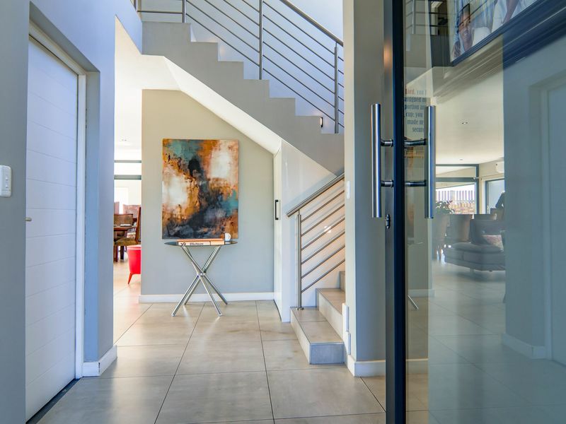 Modern entrance hall featuring tiled flooring, a contemporary staircase with stainless steel balustrades, and a glass-panelled front door leading into the home.