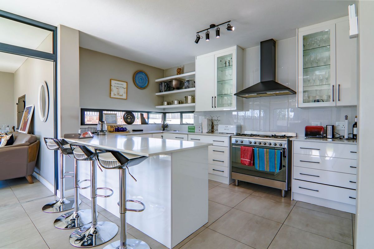 Modern kitchen featuring white cabinetry, quartz countertops, a central island, gas stove with extractor fan, and sleek tiled flooring.