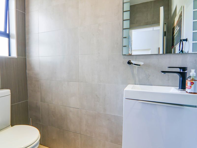 Modern bathroom featuring large format grey wall tiles, a sleek white vanity with a black mixer tap, and a contemporary toilet.