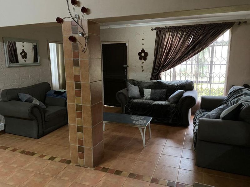 A living room area featuring tiled flooring, a central tiled support column, and windows fitted with security bars.