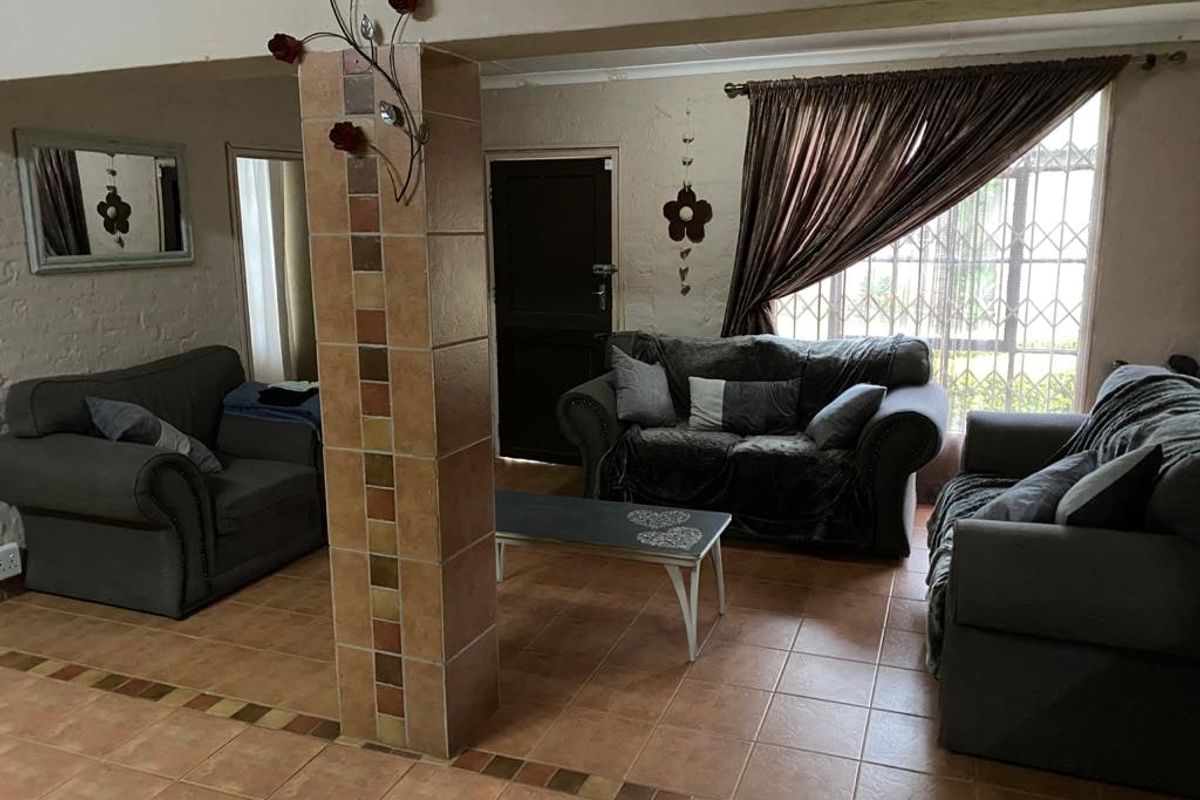 A living room area featuring tiled flooring, a central tiled support column, and windows fitted with security bars.