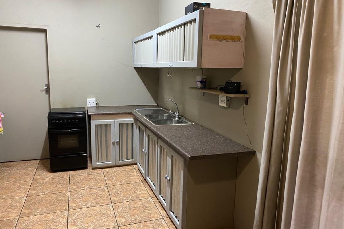 A functional kitchen area featuring built-in cabinetry, laminate countertops, a double bowl sink, and a freestanding stove with tiled flooring.