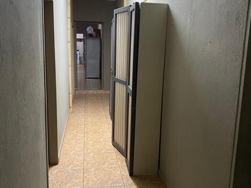 A narrow interior hallway featuring tiled flooring and basic lighting, currently showing signs of unfinished wall construction and missing trim elements.