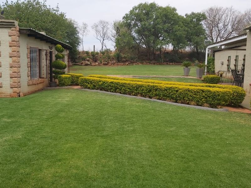 A well-maintained rear garden area featuring a lush lawn, manicured hedges, and stone-clad building exteriors with security bars on windows.