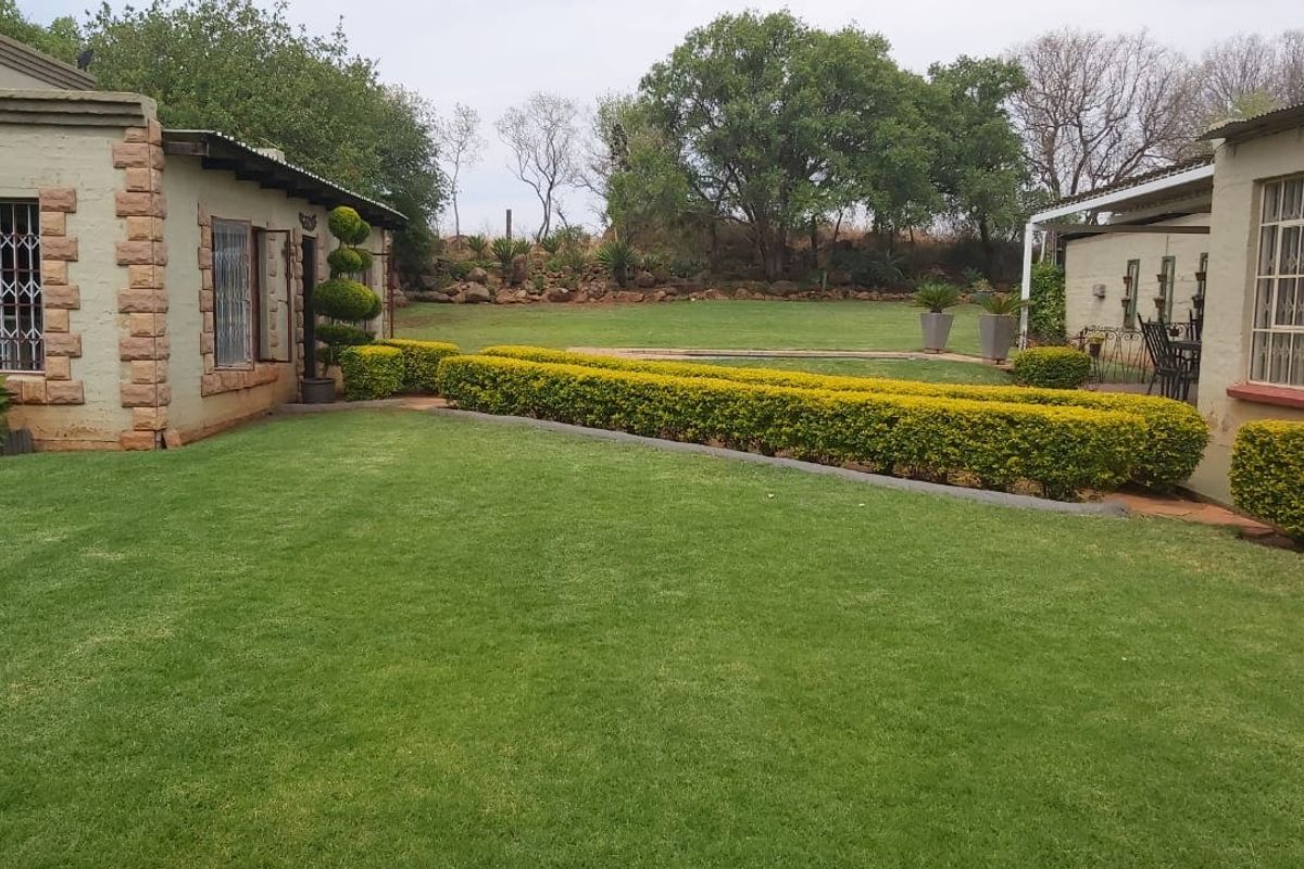 A well-maintained rear garden area featuring a lush lawn, manicured hedges, and stone-clad building exteriors with security bars on windows.