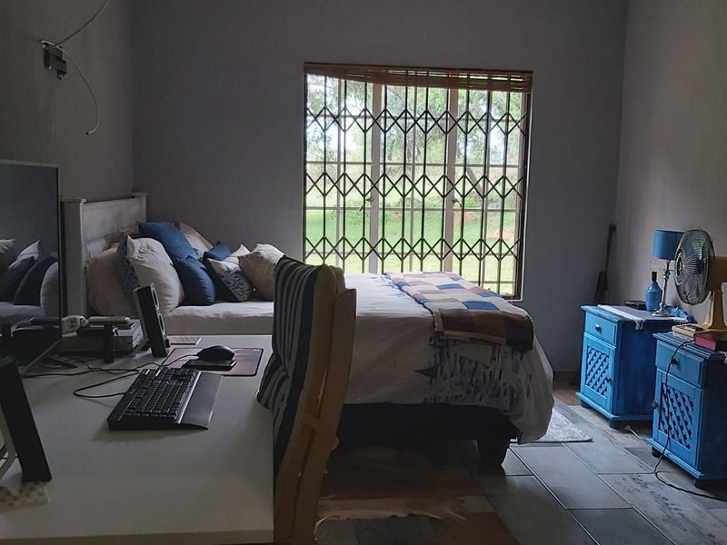 A bedroom featuring tiled flooring and a window fitted with a security gate, currently utilized as a combined sleeping and workspace area.