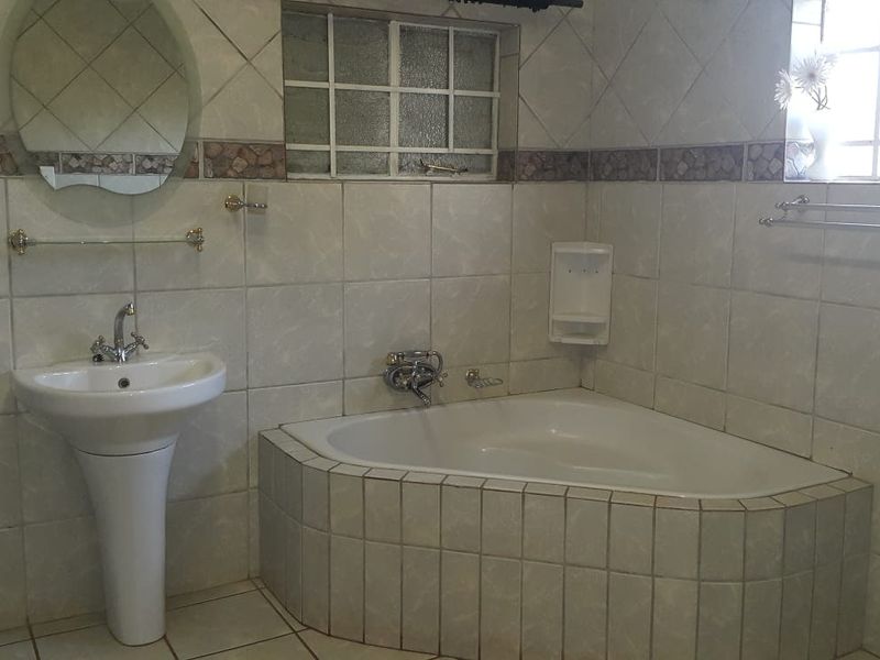 A functional bathroom featuring a corner bathtub, pedestal basin, and full-height wall tiling, offering a classic layout ready for modern updates.