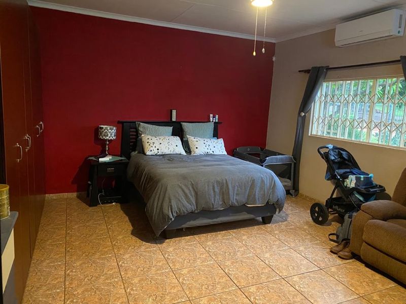 Spacious bedroom featuring tiled flooring, built-in cupboards, and a wall-mounted air conditioning unit, providing a functional and comfortable living space.