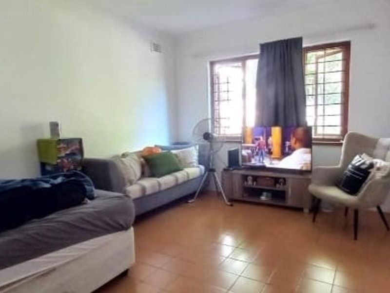 A functional bedroom featuring tiled flooring, built-in cupboards, and security bars on the windows, providing a basic and practical living space.