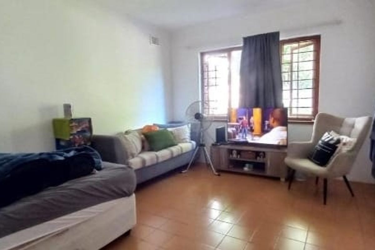 A functional bedroom featuring tiled flooring, built-in cupboards, and security bars on the windows, providing a basic and practical living space.