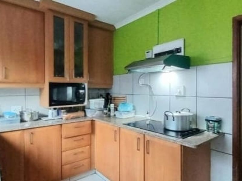 Functional kitchen featuring wooden cabinetry, laminate countertops, tiled backsplash, and integrated appliances including a hob and extractor fan.
