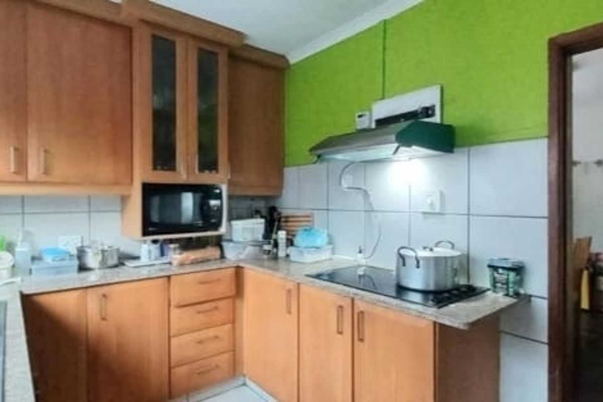 Functional kitchen featuring wooden cabinetry, laminate countertops, tiled backsplash, and integrated appliances including a hob and extractor fan.