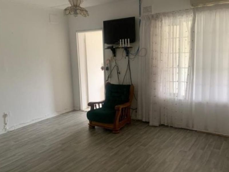 A living room featuring laminate flooring and an air conditioning unit, currently requiring cosmetic updates and better cable management.