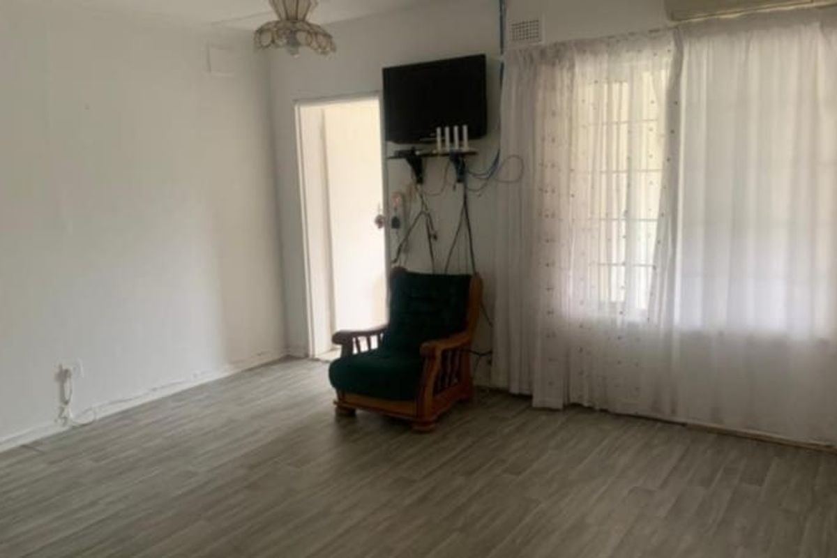 A living room featuring laminate flooring and an air conditioning unit, currently requiring cosmetic updates and better cable management.