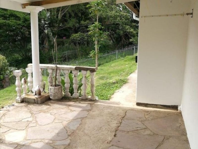 A covered outdoor patio area featuring stone paving and a classic balustrade, overlooking a garden space.