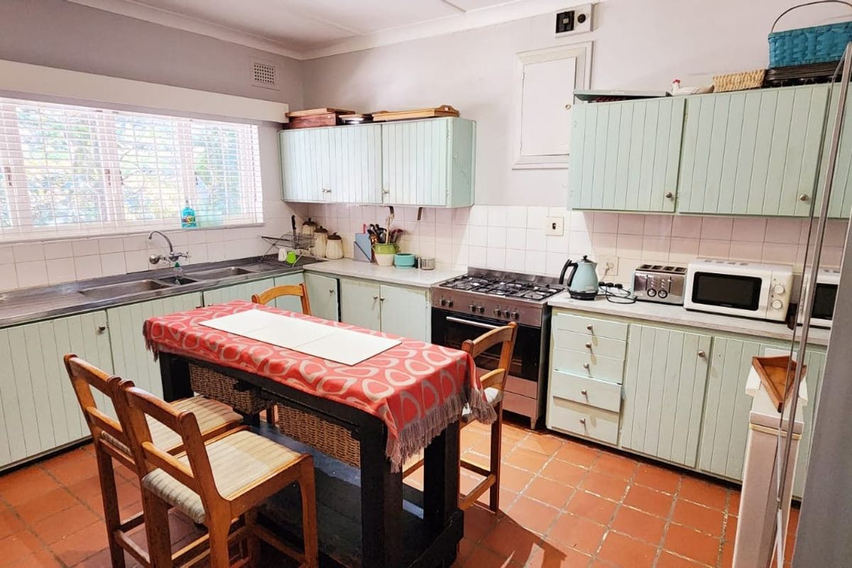 A functional kitchen featuring light green cabinetry, a gas stove, tiled backsplash, and terracotta flooring, offering a classic layout with ample storage space.