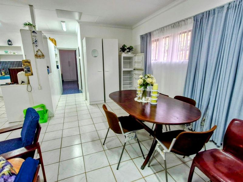 Open-plan living and dining area featuring tiled flooring and an adjacent kitchen with built-in cabinetry and tiled backsplash.