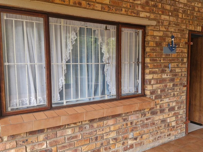 A covered patio area featuring face brick walls, tiled flooring, and timber-framed windows secured with metal burglar bars.