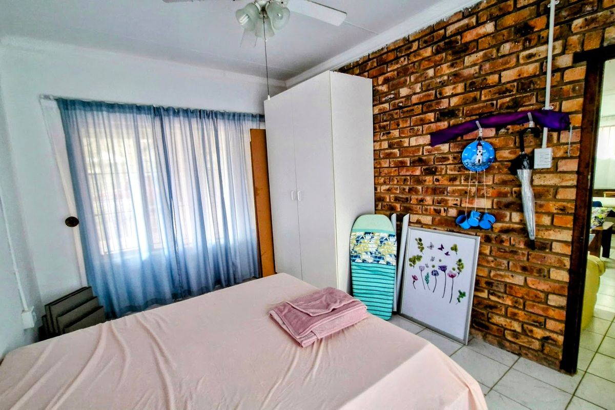Bedroom featuring an exposed brick feature wall, tiled flooring, a ceiling fan, and a built-in wardrobe.
