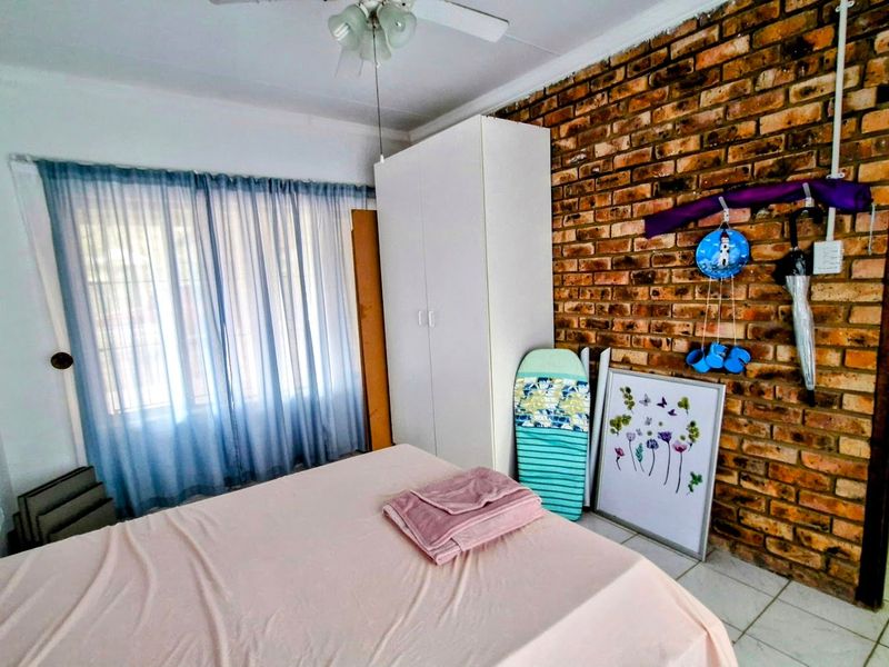 Bedroom featuring an exposed brick feature wall, tiled flooring, a ceiling fan, and a built-in wardrobe.