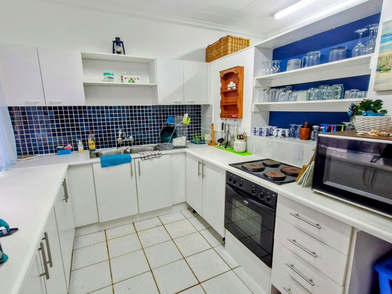 A functional kitchen featuring white cabinetry, a double basin sink, electric hob, built-in oven, and blue tiled backsplash with open shelving.