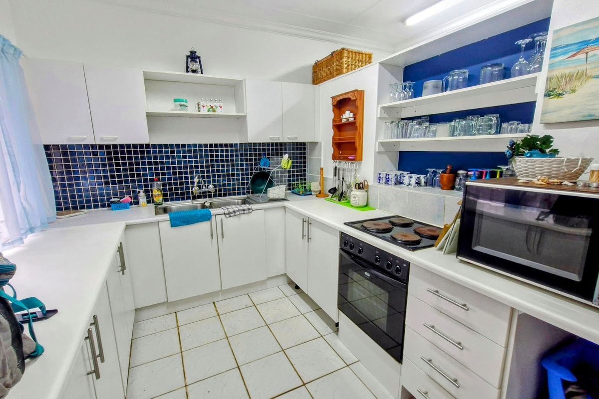 A functional kitchen featuring white cabinetry, a double basin sink, electric hob, built-in oven, and blue tiled backsplash with open shelving.