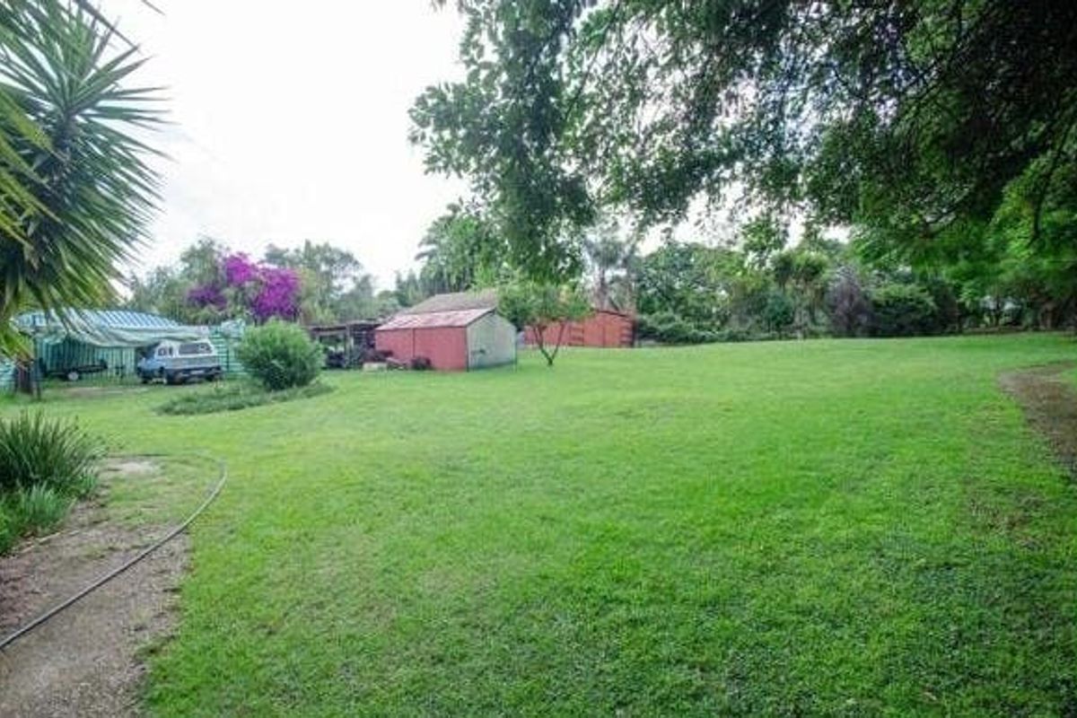 A spacious, grassed residential garden area featuring mature trees and existing outbuildings on the property.