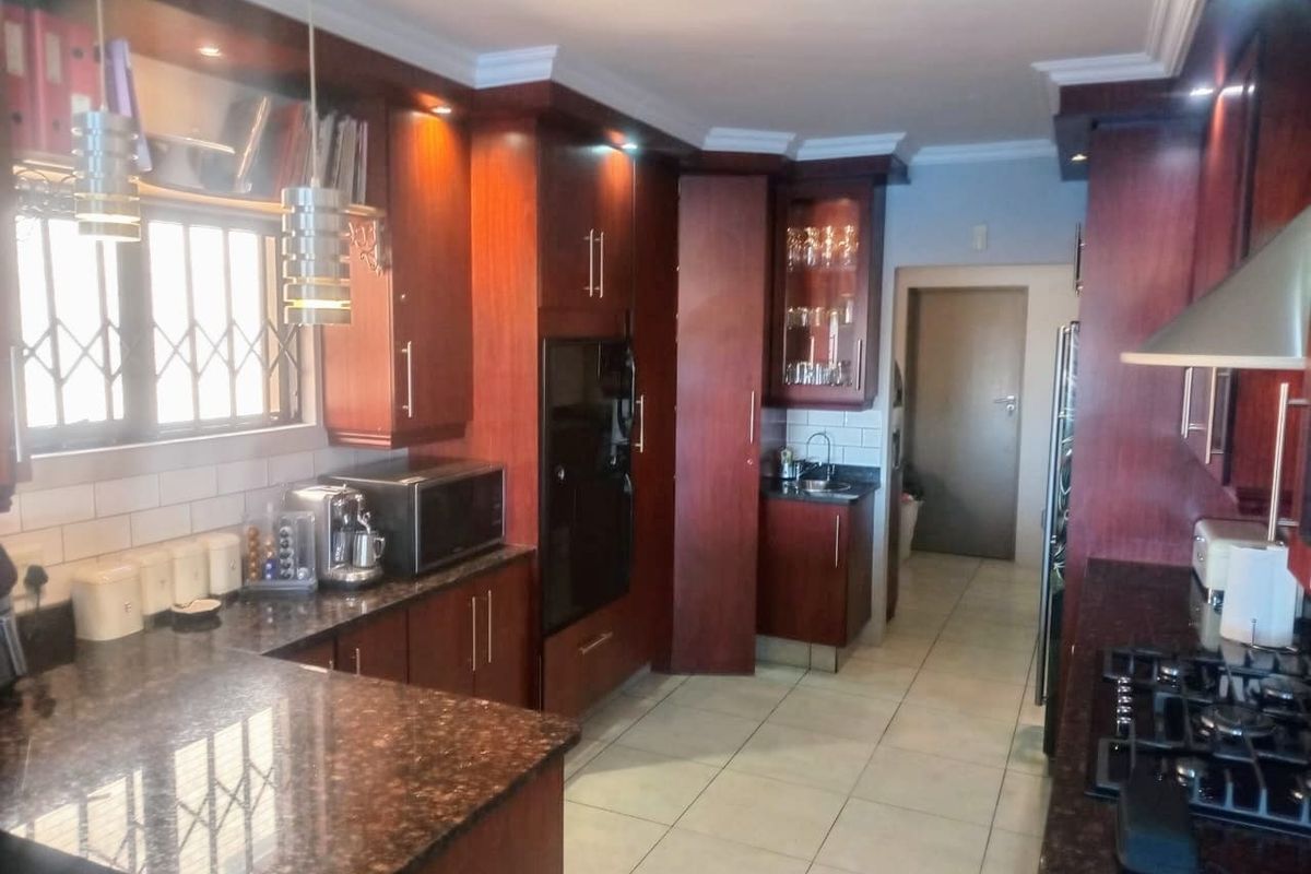 A well-maintained kitchen featuring dark wood cabinetry, granite countertops, a built-in oven, and a gas hob with an extractor fan.