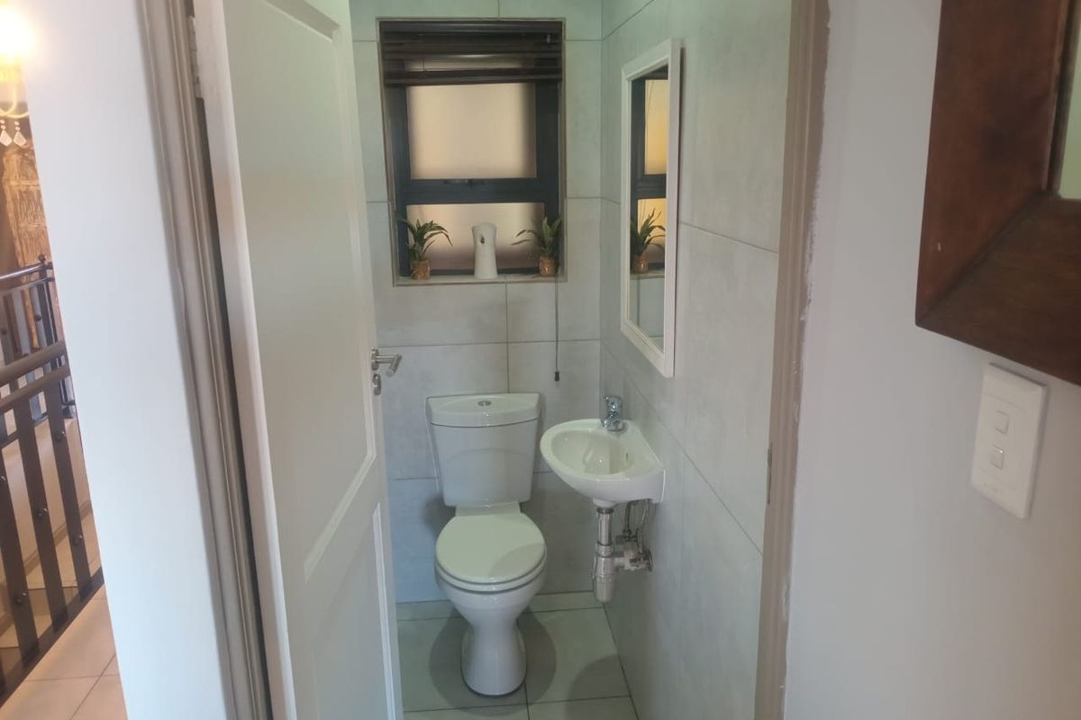A compact guest cloakroom featuring modern floor-to-ceiling tiling, a wall-mounted basin, and a standard toilet.