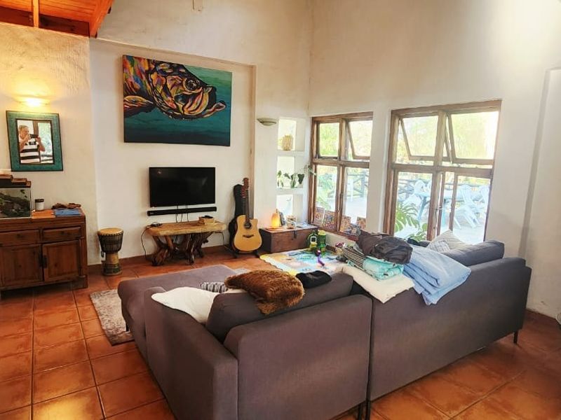 A living room featuring high ceilings with exposed timber beams, terracotta tiled flooring, and large casement windows allowing natural light.
