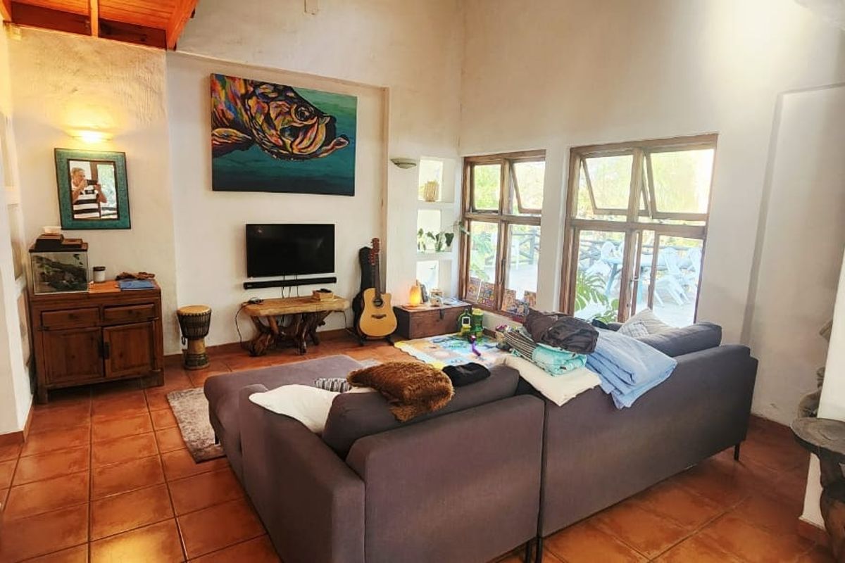 A living room featuring high ceilings with exposed timber beams, terracotta tiled flooring, and large casement windows allowing natural light.